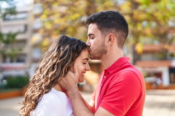 Fototapeta premium Young hispanic couple smiling confident hugging each other and kissing at park