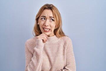 Hispanic woman standing over blue background thinking worried about a question, concerned and nervous with hand on chin