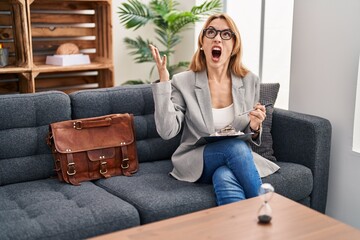 Hispanic woman working at consultation office crazy and mad shouting and yelling with aggressive...