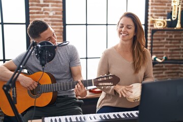 Man and woman musicians playing classical guitar and tambourine at music studio - obrazy, fototapety, plakaty