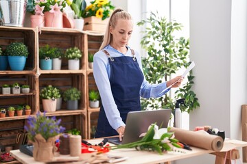 Young blonde woman florist using laptop reading document at florist
