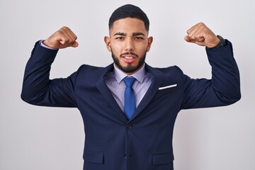 Young hispanic man wearing business suit and tie showing arms muscles smiling proud. fitness concept.