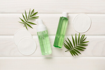 Foaming facial cleanser and micellar water with eco pads on wooden background, top view