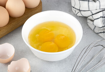 Raw eggs and whisk on a gray background, top view. Pie or cake recipe, breakfast concept, top view.