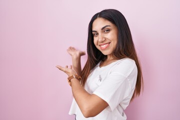 Young arab woman standing over pink background inviting to enter smiling natural with open hand