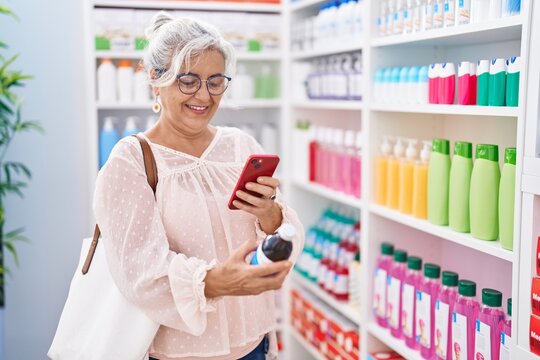 Middle age grey-haired woman customer make photo by smartphone to medicine bottle at pharmacy