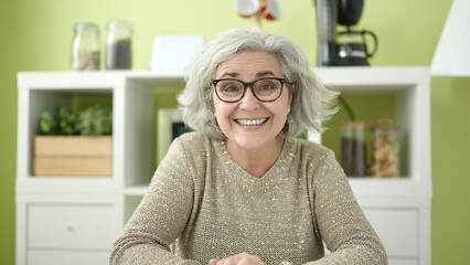 Middle age woman with grey hair smiling confident sitting on table at home