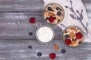 Homemade granola with nuts, raspberries and blueberries, yogurt on a gray whitewashed rustic table, top view, copy space. Healthy breakfast
