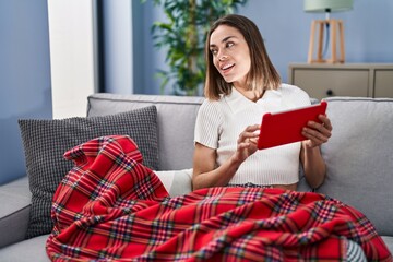 Young beautiful hispanic woman using touchpad sitting on sofa at home