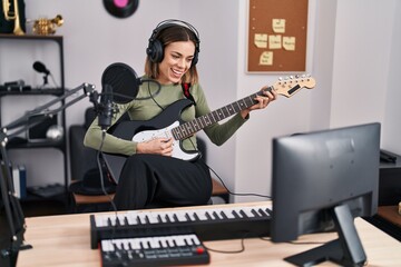 Young beautiful hispanic woman musician playing electrical guitar at music studio
