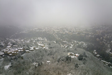Aerial foggy landscape with mountain cliffs covered with fresh fallen snow during heavy snowfall in winter mountain forest on cold quiet day