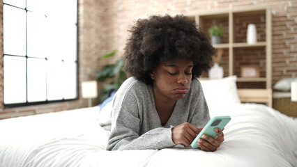 Fototapeta na wymiar African american woman using smartphone lying on bed at bedroom