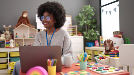 African american woman preschool teacher smiling confident using laptop at kindergarten