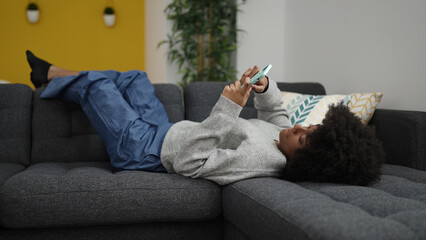 African american woman using smartphone lying on sofa at home