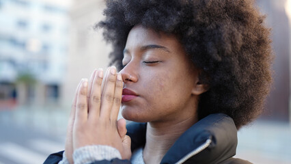Fototapeta na wymiar African american woman praying with closed eyes at street