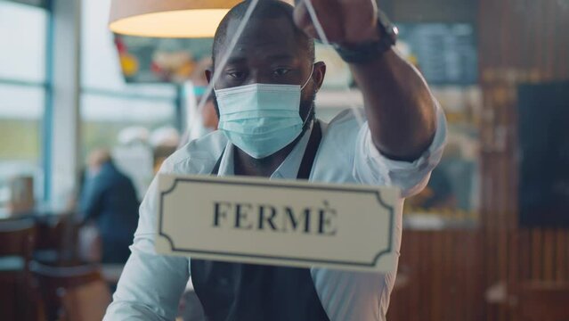 African-American waiter in mask turn ouvert ferme sign on cafe door. Realtime