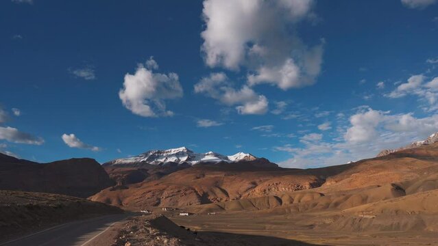 4K shot of road going towards snow capped mountains in Spiti Valley, Himachal Pradesh, India. Himalayan Mountains with peaks covered with snow and clouds in sky. Nature landscape.