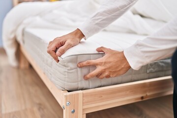Young hispanic man touching mattress at bedroom