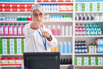 Middle age woman with tattoos working at pharmacy drugstore punching fist to fight, aggressive and...