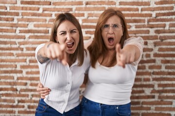 Hispanic mother and daughter wearing casual white t shirt pointing displeased and frustrated to the camera, angry and furious with you