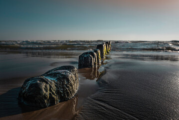Ruins of an old bridge to the sea washed out by water and sand with a very calm sea in background