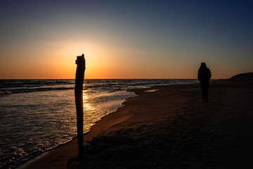 A woman walking away to the distance by the beach during beautiful red sunset