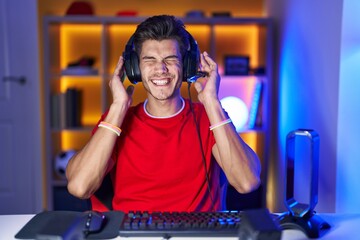 Young hispanic man playing video games covering ears with fingers with annoyed expression for the...