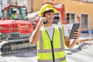 Young hispanic man architect talking on smartphone using touchpad at park