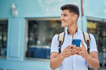 Young hispanic man student using smartphone at street