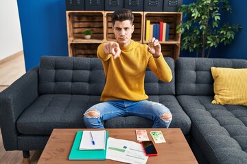 Young hispanic man holding bitcoin virtual money pointing with finger to the camera and to you, confident gesture looking serious