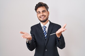 Young hispanic man with tattoos wearing business suit and tie smiling cheerful offering hands giving assistance and acceptance.