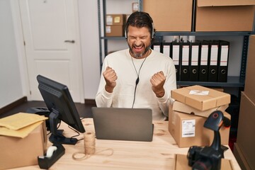 Handsome middle age man working at small business ecommerce wearing headset screaming proud, celebrating victory and success very excited with raised arms