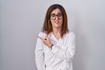 Brunette woman standing over white isolated background pointing aside worried and nervous with forefinger, concerned and surprised expression