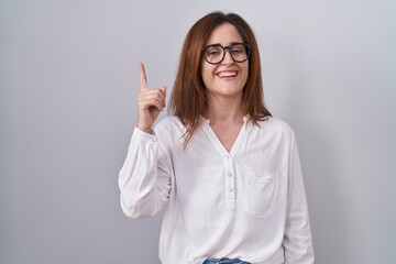 Brunette woman standing over white isolated background pointing finger up with successful idea. exited and happy. number one.
