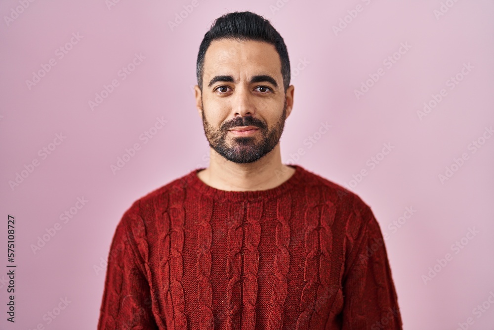 Poster Young hispanic man with beard wearing casual sweater over pink background relaxed with serious expression on face. simple and natural looking at the camera.