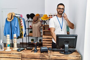 Young hispanic man shopkeeper talking on the smartphone working at clothing store