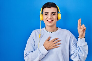 Non binary person listening to music using headphones smiling swearing with hand on chest and...