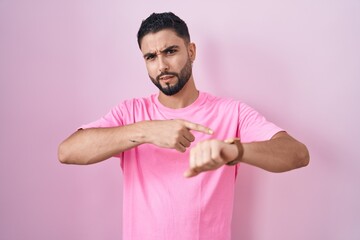 Hispanic young man standing over pink background in hurry pointing to watch time, impatience, upset...