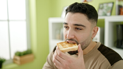 Young arab man eating toast sitting on table at home