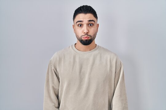 Young handsome man standing over isolated background puffing cheeks with funny face. mouth inflated with air, crazy expression.
