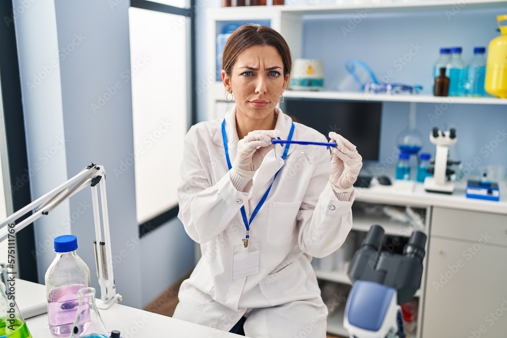 Sticker young brunette woman working at scientist laboratory wearing safety glasses skeptic and nervous, fro