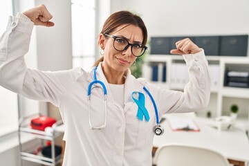 Young brunette doctor woman wearing stethoscope at the clinic showing arms muscles smiling proud. fitness concept.