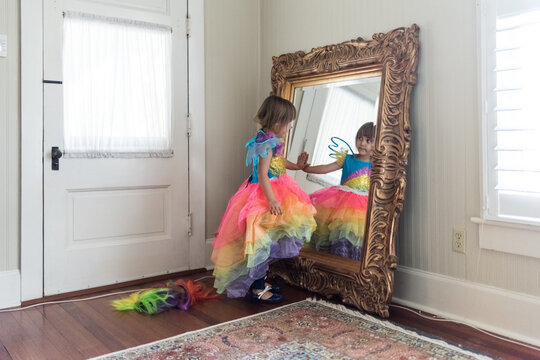 Unposed Young girl playing dress up, looking at her reflection in a mirror