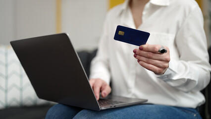 Young blonde woman using laptop and credit card sitting on sofa at home