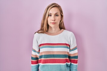 Young blonde woman standing over pink background relaxed with serious expression on face. simple and natural looking at the camera.