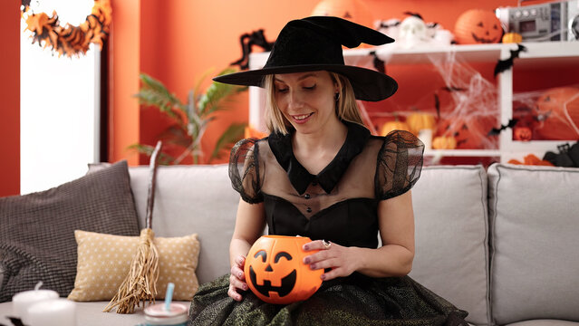 Young blonde woman having halloween party holding pumpkin basket at home
