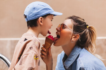 Woman with her son enjoying family time walking in the city together on a sunny day, eating ice cream. Happy family parent with little child boy kid enjoy outdoor lifestyle. Mum and sun lick gelato.