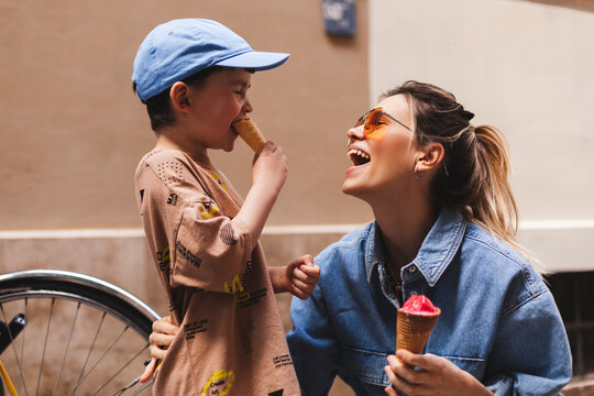 Woman with her son enjoying family time walking in the city together on a sunny day, eating ice cream. Happy family parent with little child boy kid enjoy outdoor lifestyle. Mum and sun lick gelato