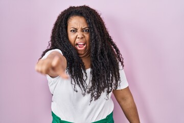 Plus size hispanic woman standing over pink background pointing displeased and frustrated to the camera, angry and furious with you