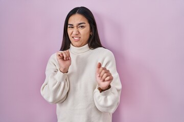 Young south asian woman standing over pink background disgusted expression, displeased and fearful doing disgust face because aversion reaction. - obrazy, fototapety, plakaty